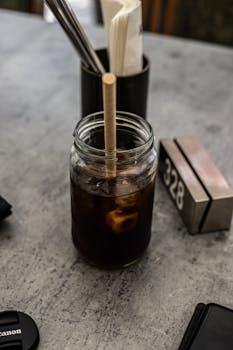 Iced coffee served in a glass jar with a paper straw on a rustic cafe table.