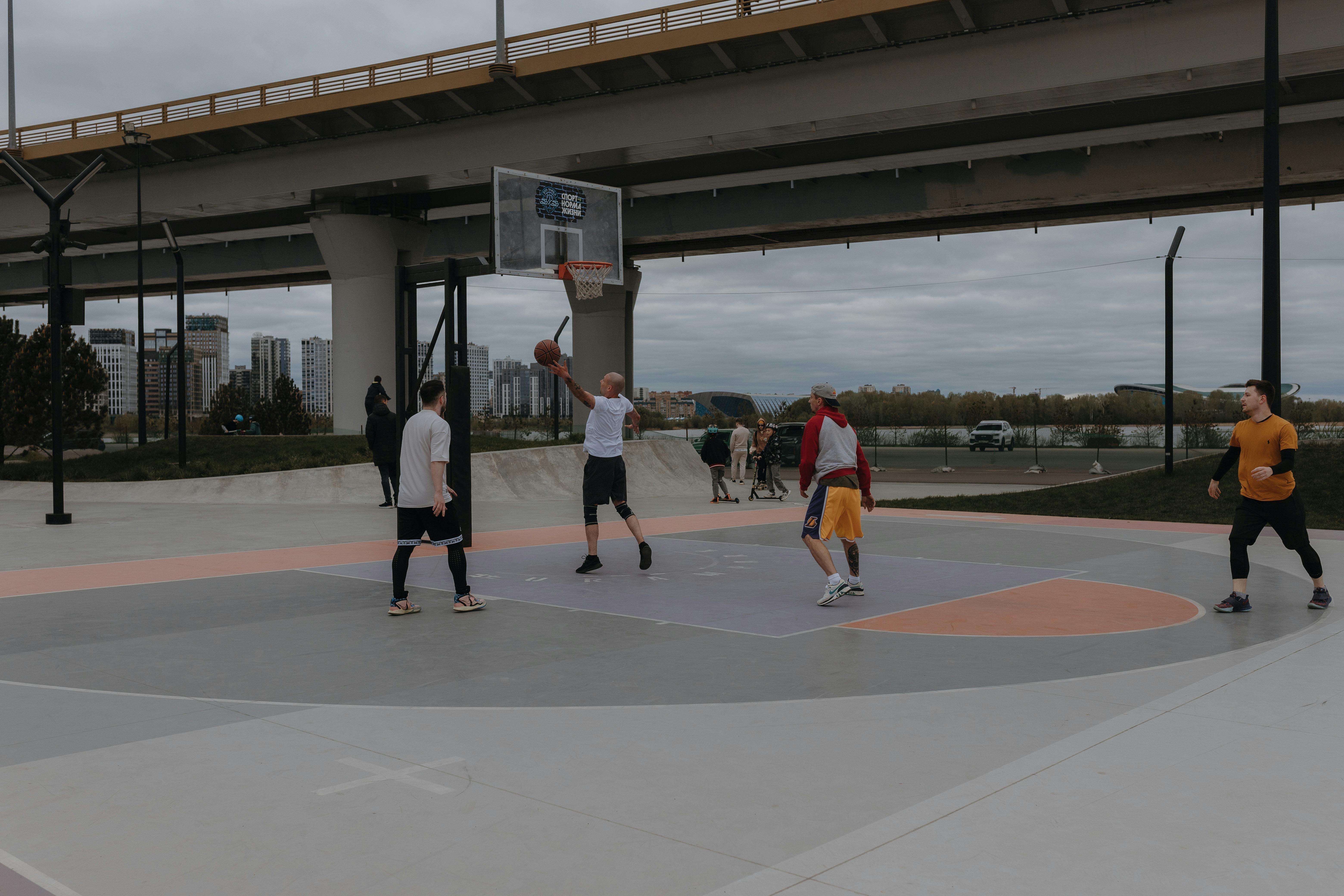 NCAA Basketball photo featuring Men playing basketball on an outdoor court beneath a city highway bridge.