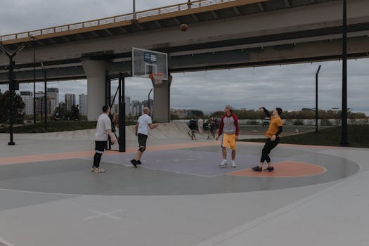 Four men playing basketball on an outdoor court under a city bridge, enjoying a recreational sport.