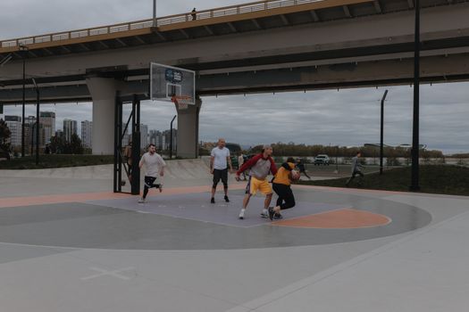 A dynamic basketball game taking place on an urban outdoor court under a bridge.