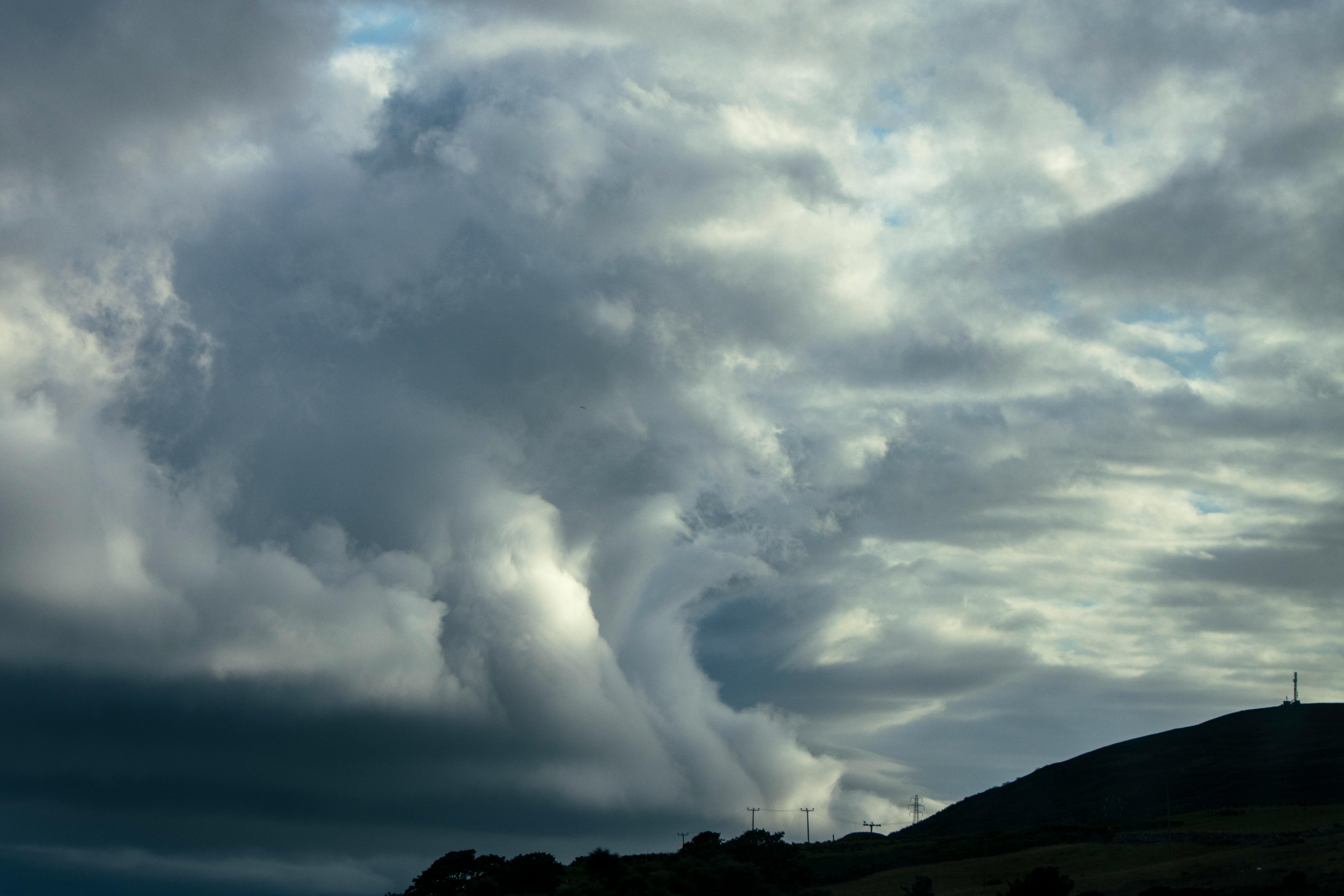 A striking cloud formation with dark stormy clouds over rolling hills, perfect for weather-related themes.