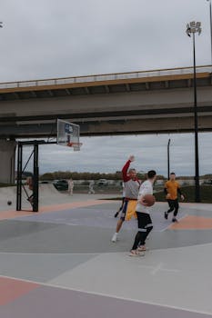 Basketball players enjoy a game under a city bridge.
