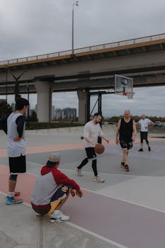 A group of men playing basketball on an outdoor court under a bridge, showcasing urban recreation.