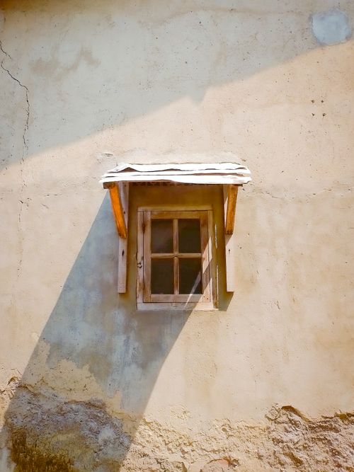 Free Rustic wooden window casting long shadows on a textured stucco wall, creating a serene architectural scene. Stock Photo