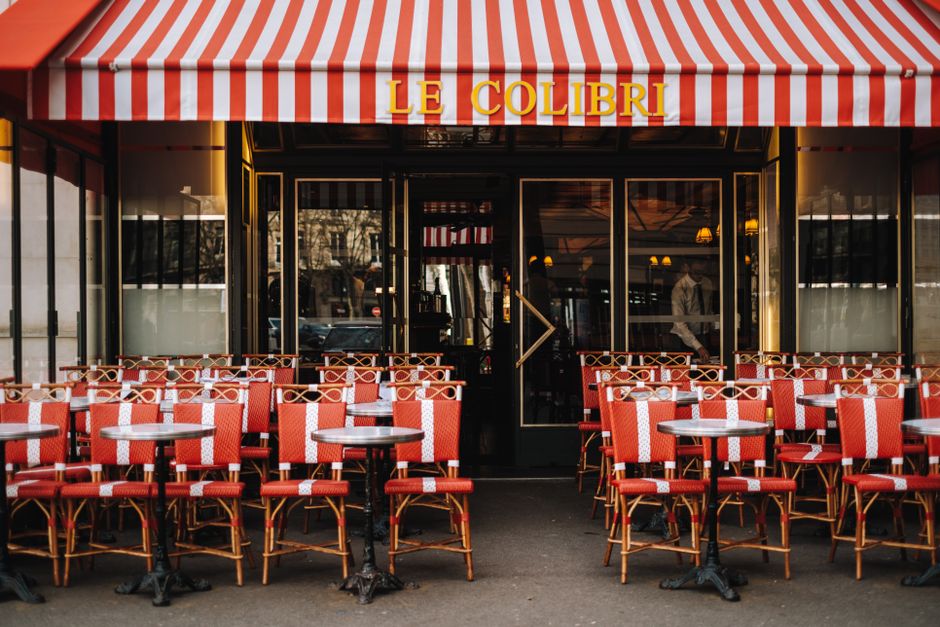 A quaint Parisian caf茅 with red-striped awning and empty outdoor seating, inviting ambiance.