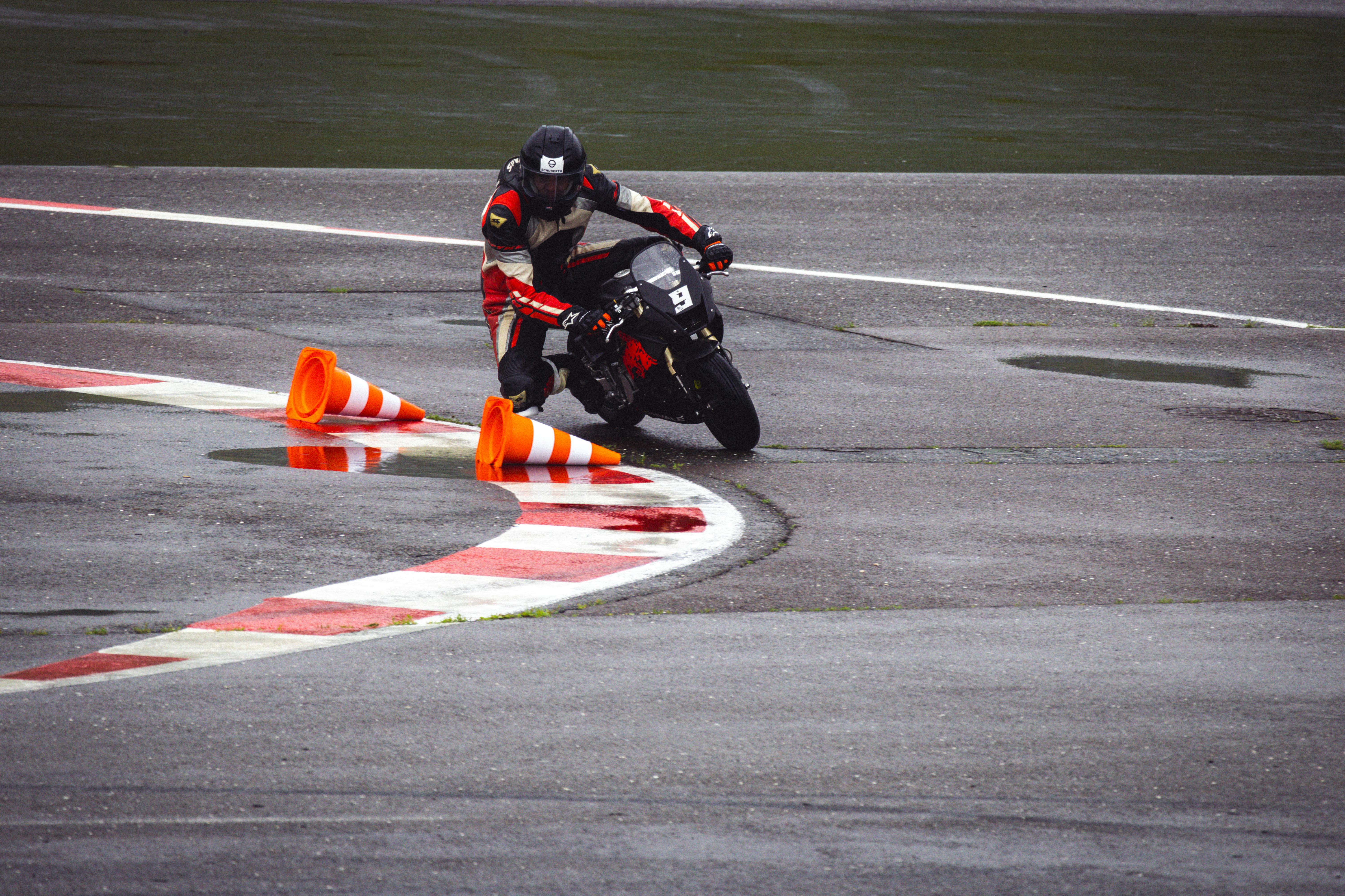 Motorcycle racer skillfully navigating a wet circuit track with traffic cones during a motorsport event.