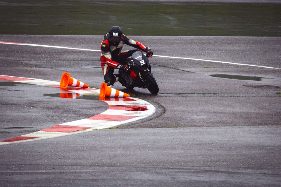Motorcycle racer skillfully navigating a wet circuit track with traffic cones during a motorsport event.