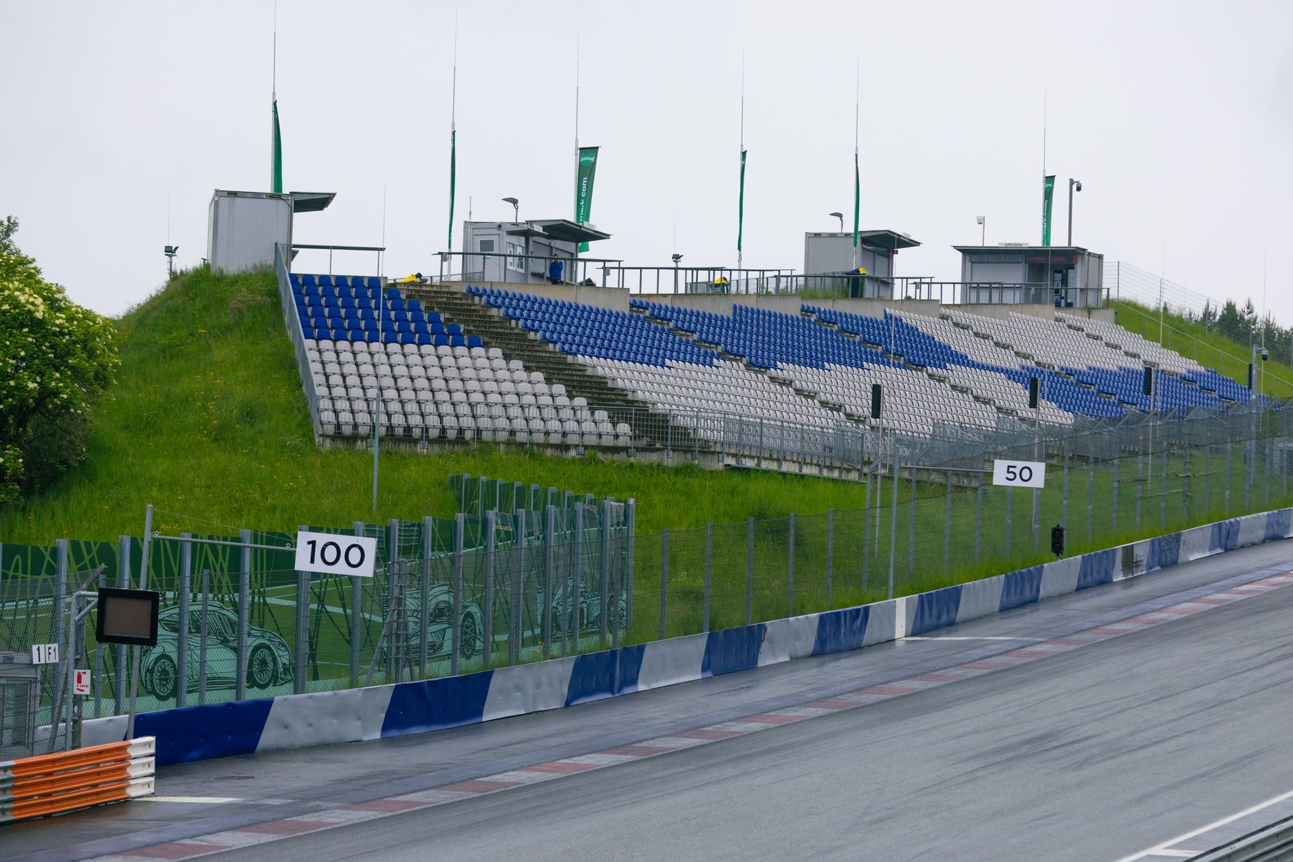 Empty grandstand at a motorsports track featuring blue and white seats, grass verge, and fencing.