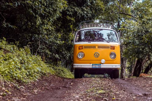 Free Classic yellow VW bus driving on a forest dirt road, capturing a sense of adventure and nostalgia. Stock Photo