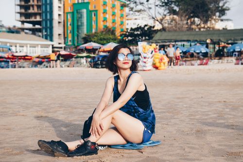 Free Woman sitting on a beach showcasing urban style with city backdrop. Stock Photo