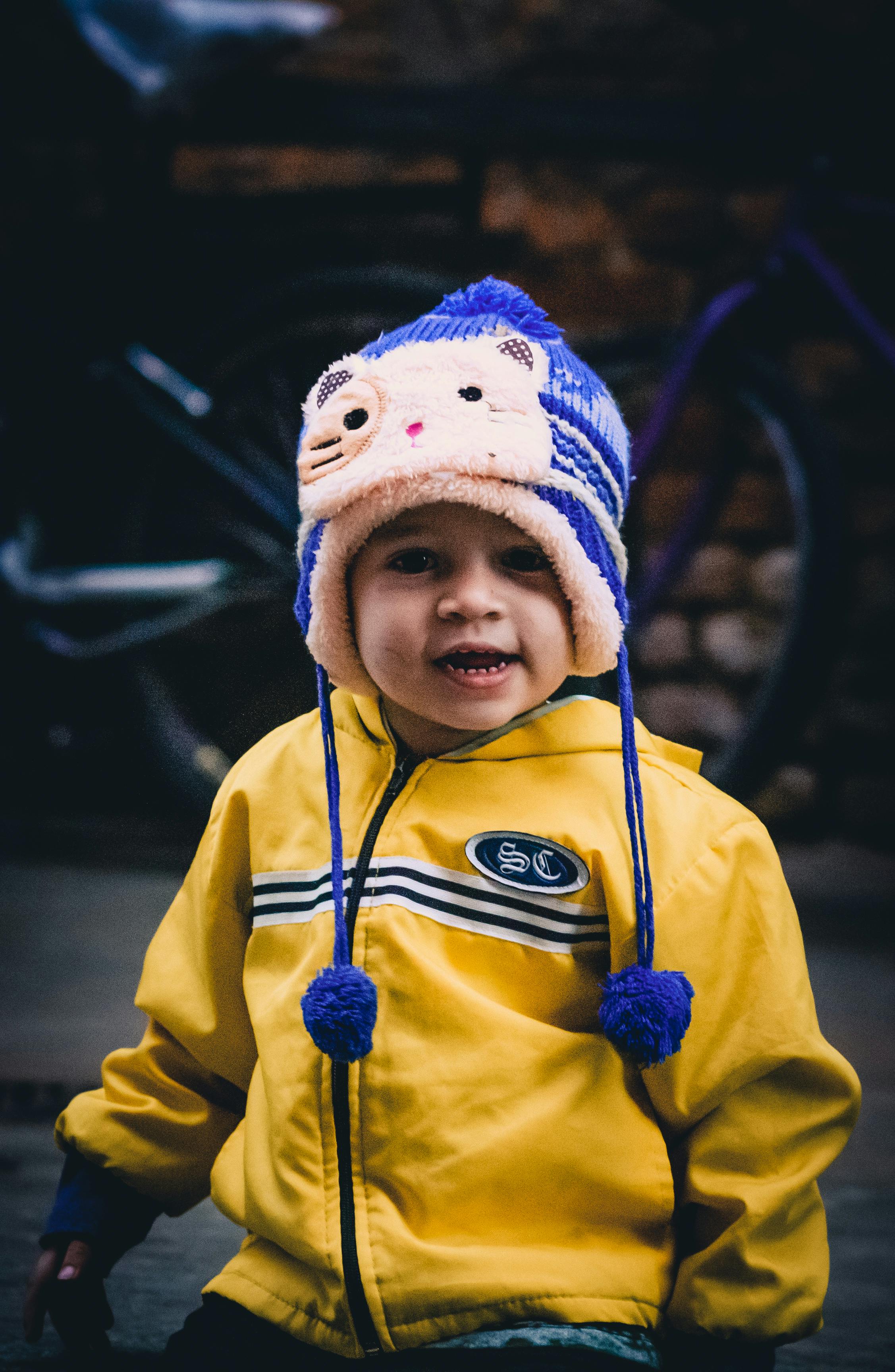 可爱的孩子戴着五颜六色的冬帽，穿着黄色夹克在户外摆姿势