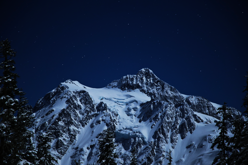 Free A breathtaking view of a snow-covered mountain peak beneath a tranquil, star-filled night sky. Stock Photo