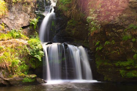Tranquil waterfall amidst lush greenery and rocky terrain in Aberlour, Scotland.