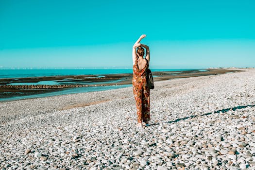 一位身着图案服装的女子站在宁静的鹅卵石海滩上，眺望着碧绿的海景