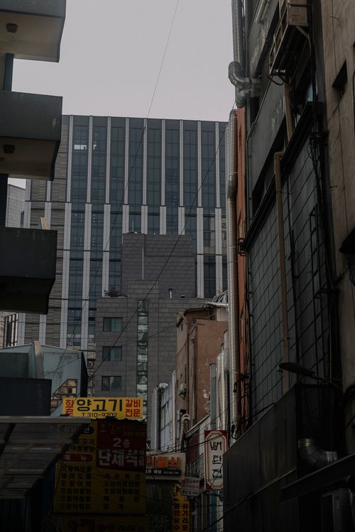 Free A view of a narrow urban alleyway bordered by tall buildings under an overcast sky. Stock Photo