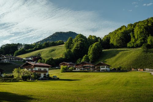Free Charming farmhouses nestled in a lush green valley with mountainous backdrop under a bright sky. Stock Photo