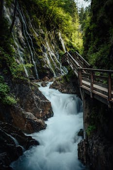 Beautiful waterfall cascading through rocks with a wooden bridge in a lush green forest setting.