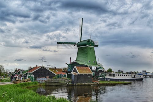 A green windmill is on a dock next to a river