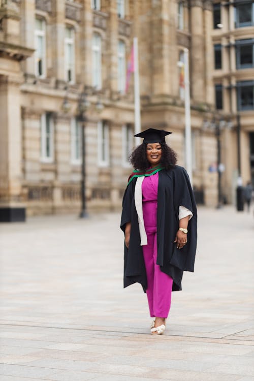 A woman in a graduation gown and cap standing in front of a building
