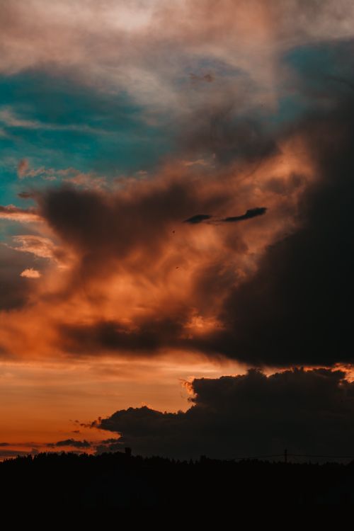 Free A stunning sunset with dramatic clouds casting vibrant hues over the horizon, creating a peaceful and scenic atmosphere. Stock Photo