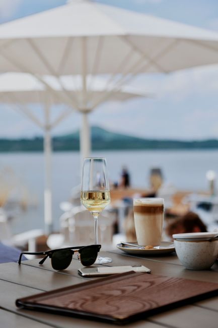 A tranquil café setting by the lake in Dresden, Germany, featuring wine and coffee on a sunny day.