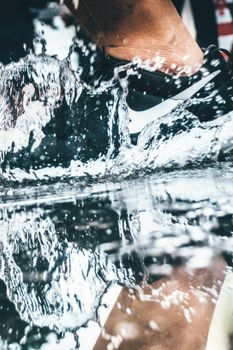 Close-up of a sneaker splashing water, capturing motion and reflection outdoors.