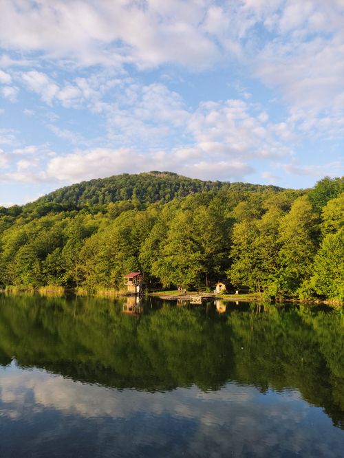 Free A beautiful landscape of a tranquil lake reflecting lush green hills and blue sky in summer. Stock Photo