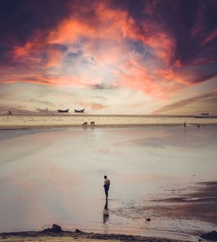 A serene beach at sunset with vibrant clouds reflecting in the tranquil water.