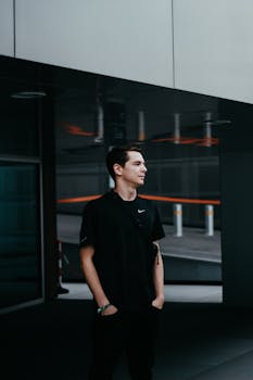 在柏林的户外，一位身着休闲黑色服装的年轻人站在反光的背景前