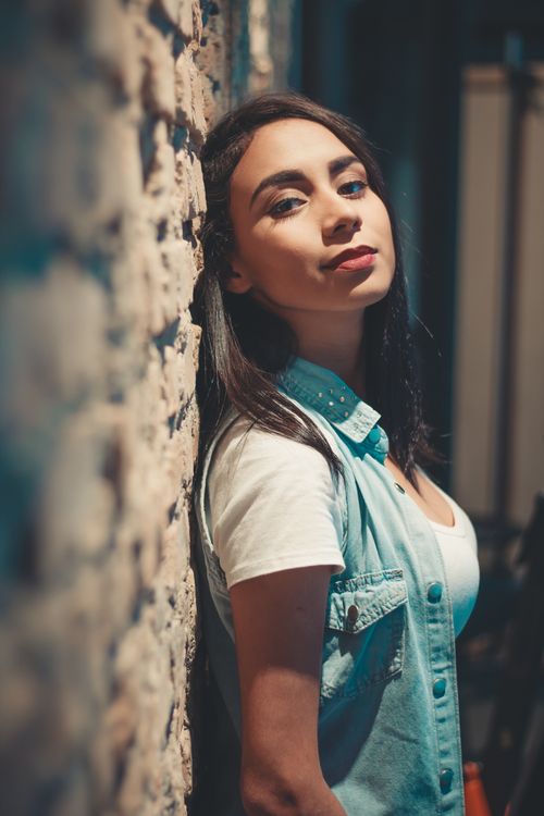 Free Portrait of a stylish young woman leaning against a textured wall, highlighting fashion and attitude. Stock Photo