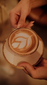 A warm close-up of a coffee cup showcasing intricate latte art being held.