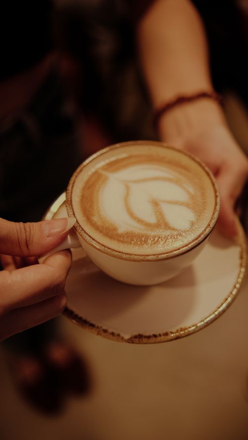 Free A woman holding a latte with intricate art in a porcelain cup and saucer. Stock Photo