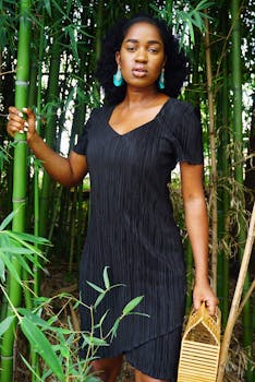 一位穿着时尚黑色连衣裙的黑人妇女在户外的竹林中优雅地摆着姿势