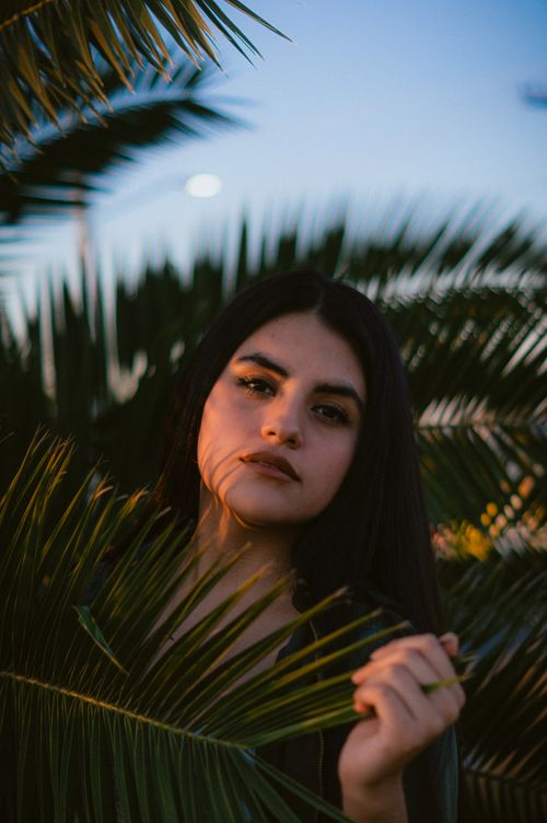 Free Striking portrait photography capturing a woman's expression surrounded by tropical palm trees. Stock Photo