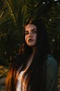 一位长发乌黑的女人肖像令人惊叹，她站在户外，身旁有棕榈叶