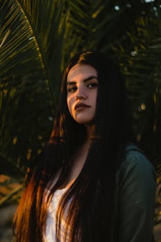 一位长发乌黑的女人肖像令人惊叹，她站在户外，身旁有棕榈叶