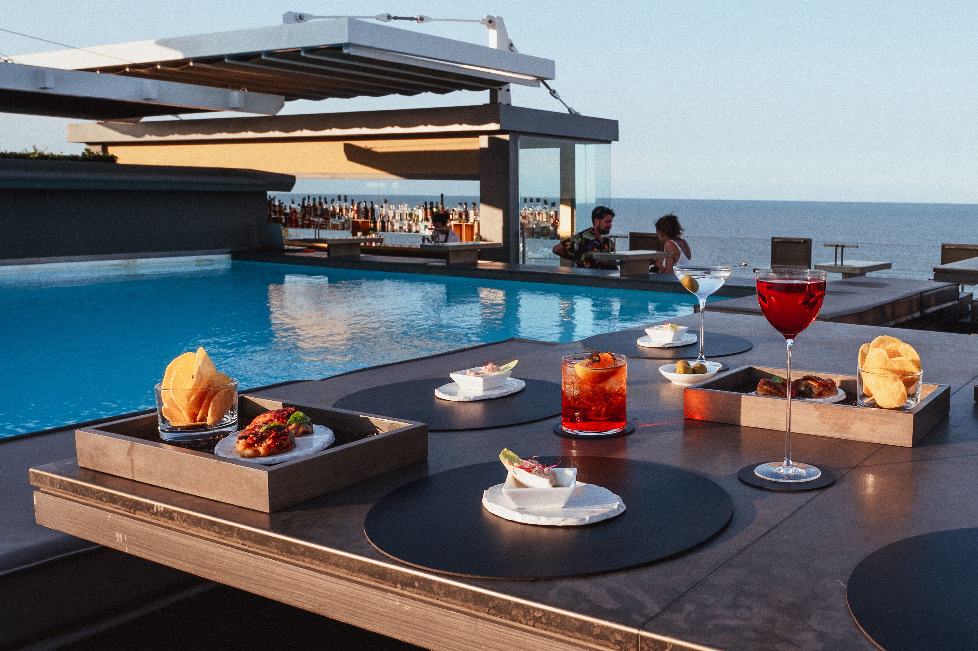 Rooftop bar with an infinity pool and daybeds overlooking the Indian Ocean at golden hour in Seminyak, Bali