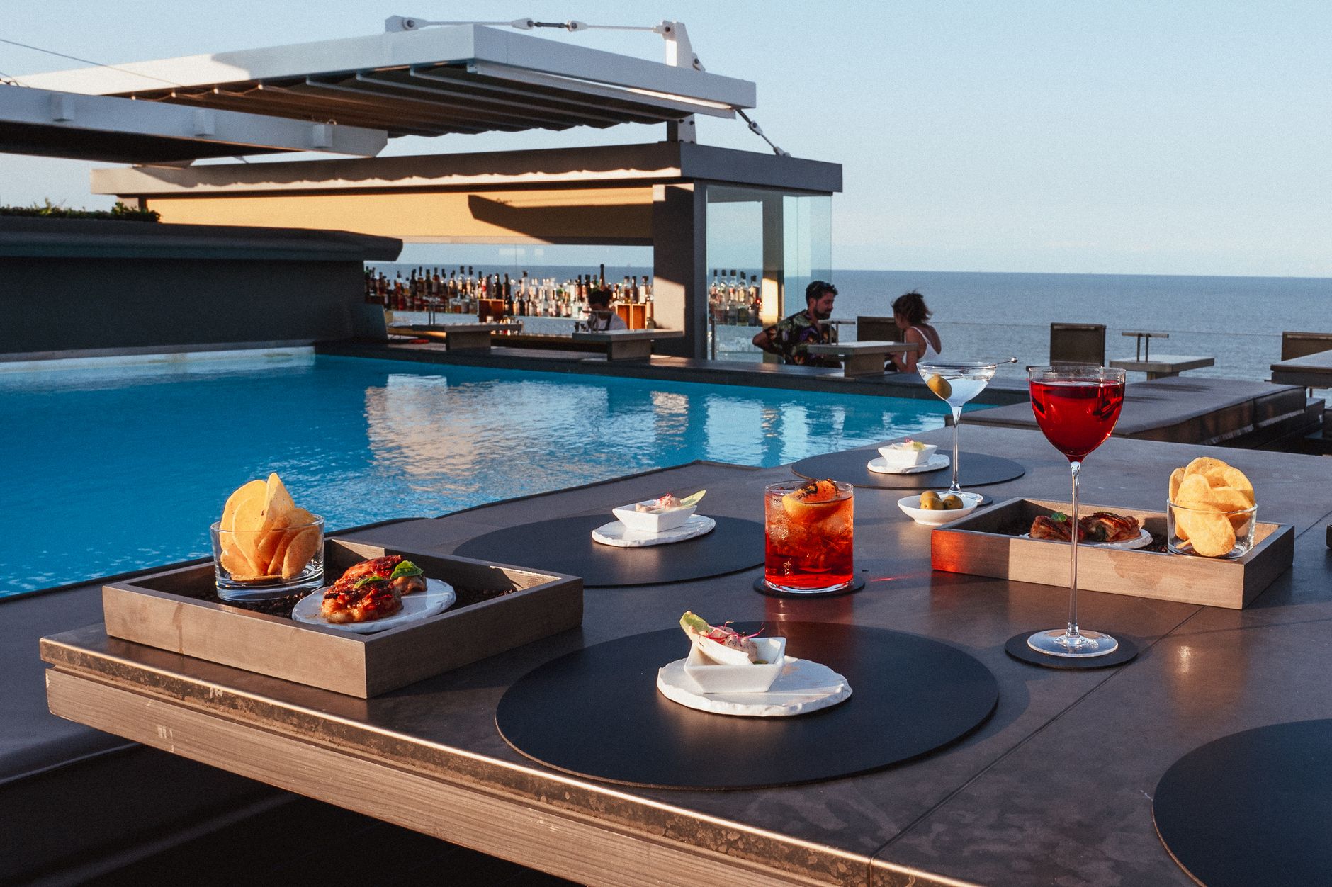 Elegant rooftop dining by the pool with sea views, featuring gourmet snacks and cocktails.