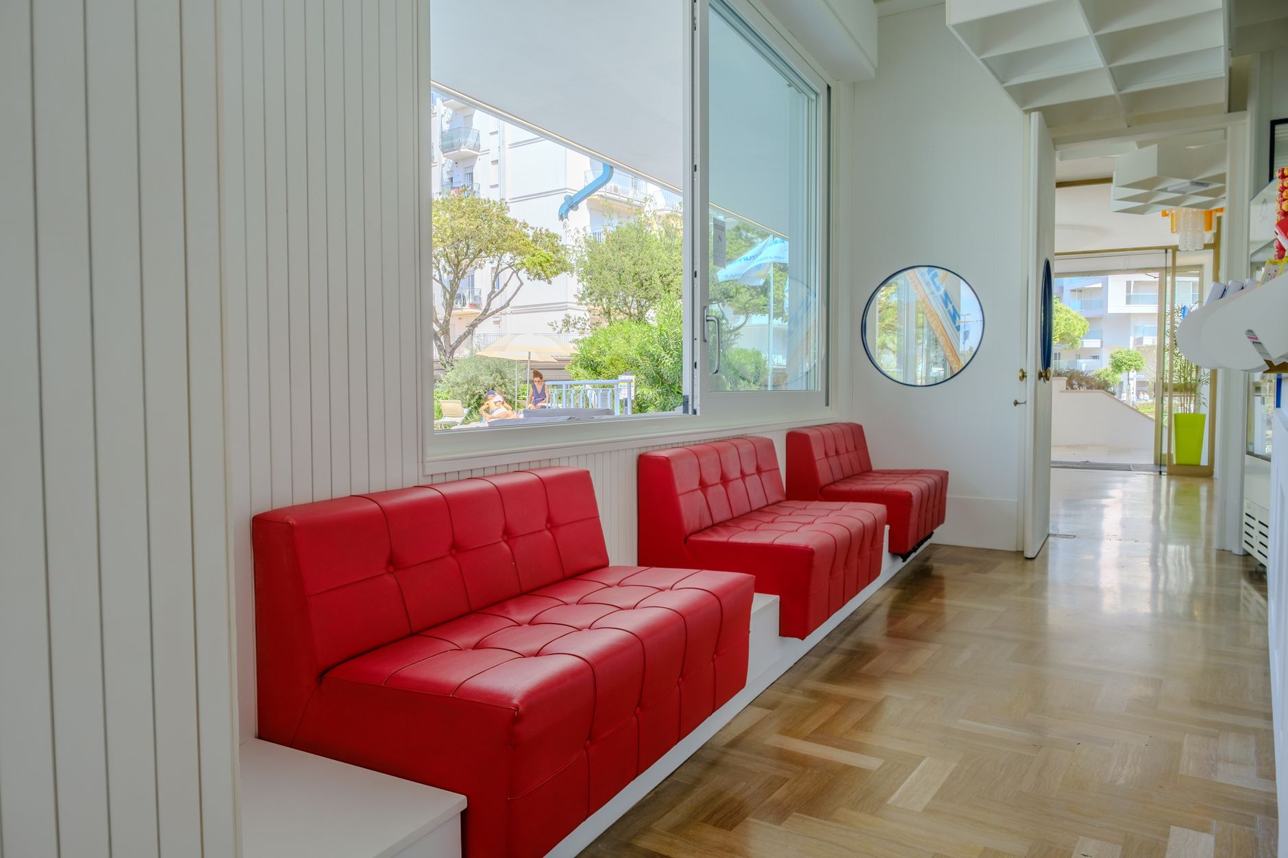 Bright lounge featuring red sofas, parquet floor, and natural lighting through large windows.