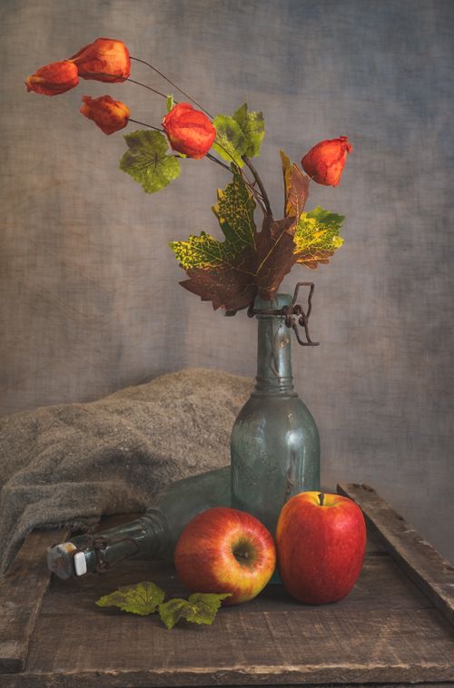 Free A classic still life featuring apples and flowers in a vintage glass bottle. Stock Photo