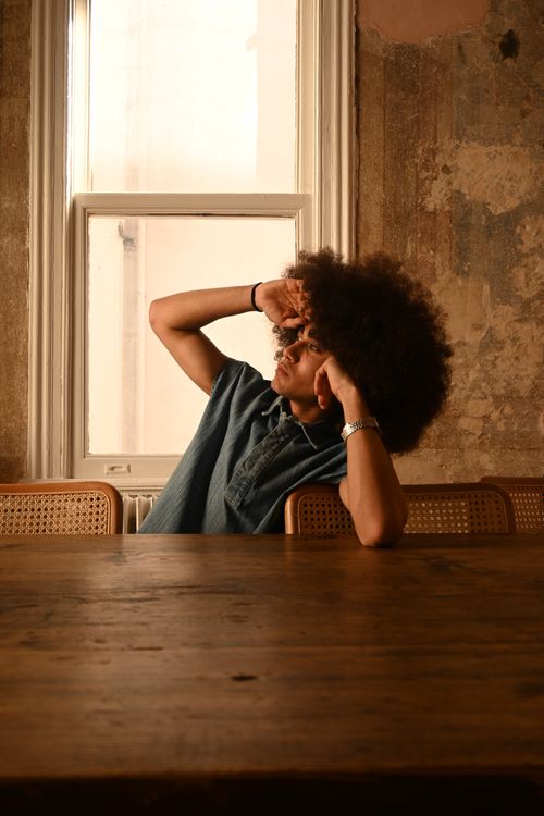 Free Stylish man with afro hair sitting by a window with rustic decor. Stock Photo