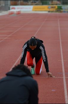 Woman athlete crouching at start line on outdoor track, focused and ready to run.