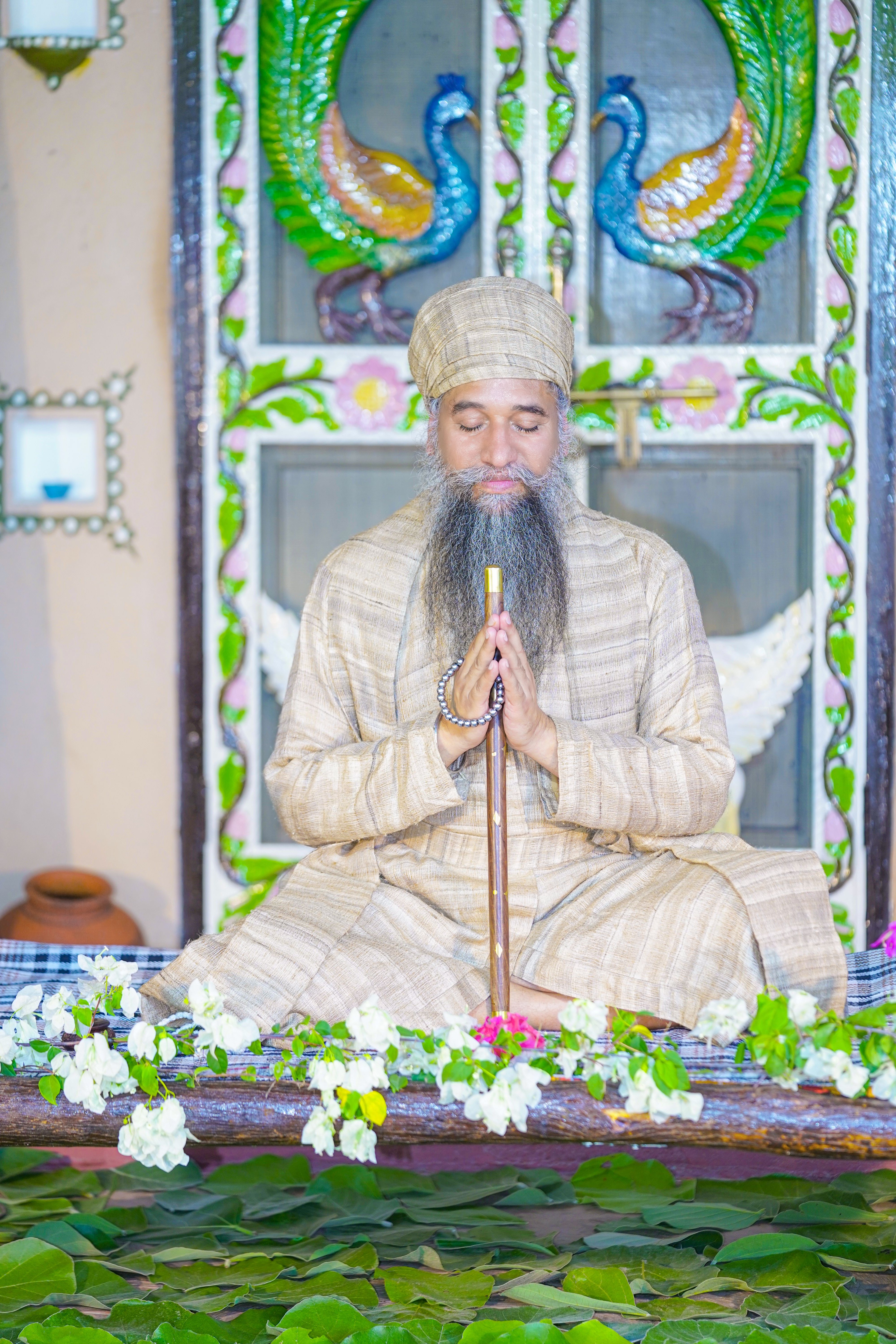 Adult man meditating in traditional Indian attire with eyes closed, surrounded by floral decorations.
