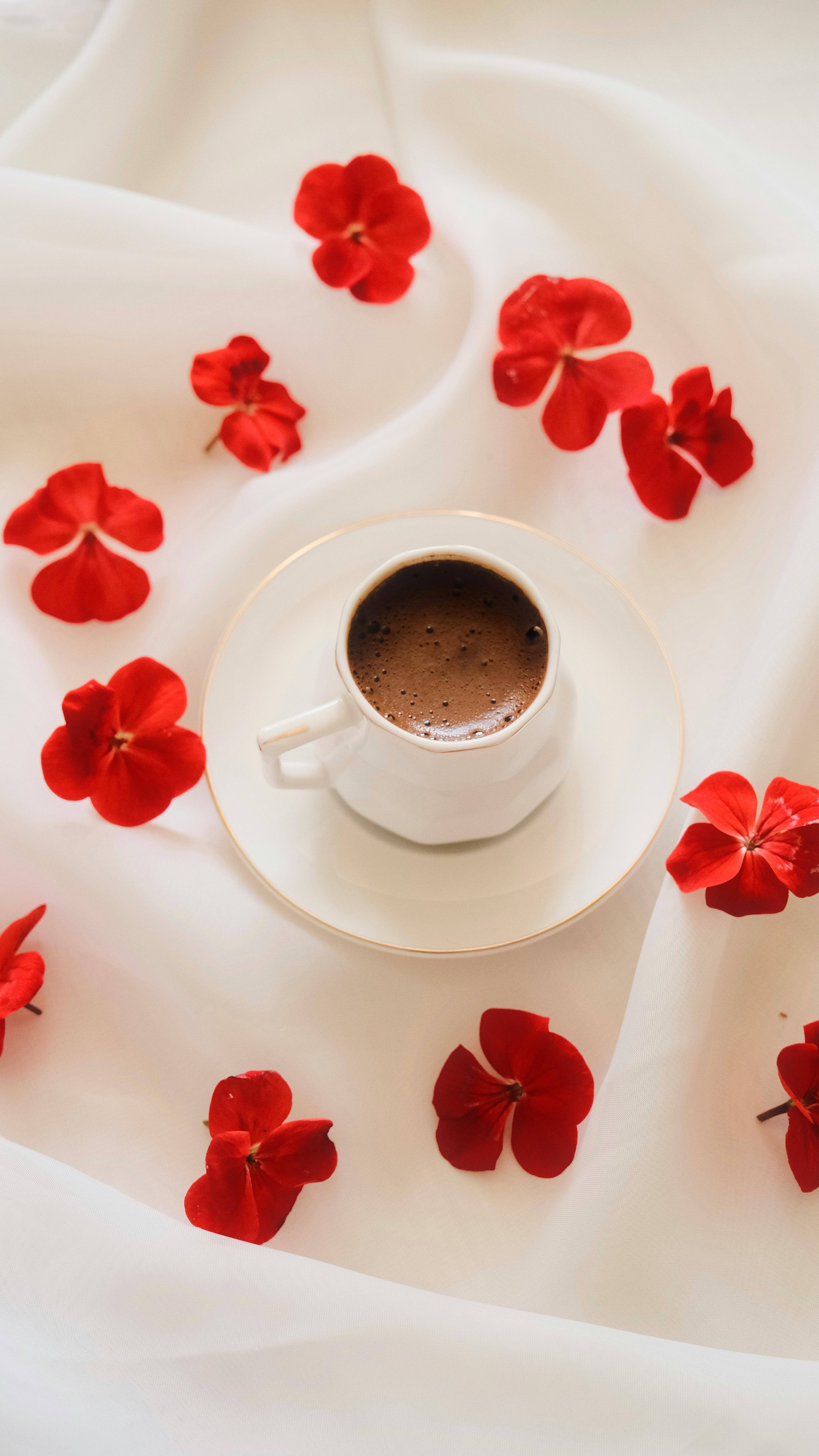 A coffee cup on a white tablecloth surrounded by bright red flowers, creating a vibrant and elegant scene.