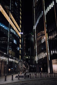 Dramatic night view of illuminated skyscrapers surrounding a striking urban sculpture.