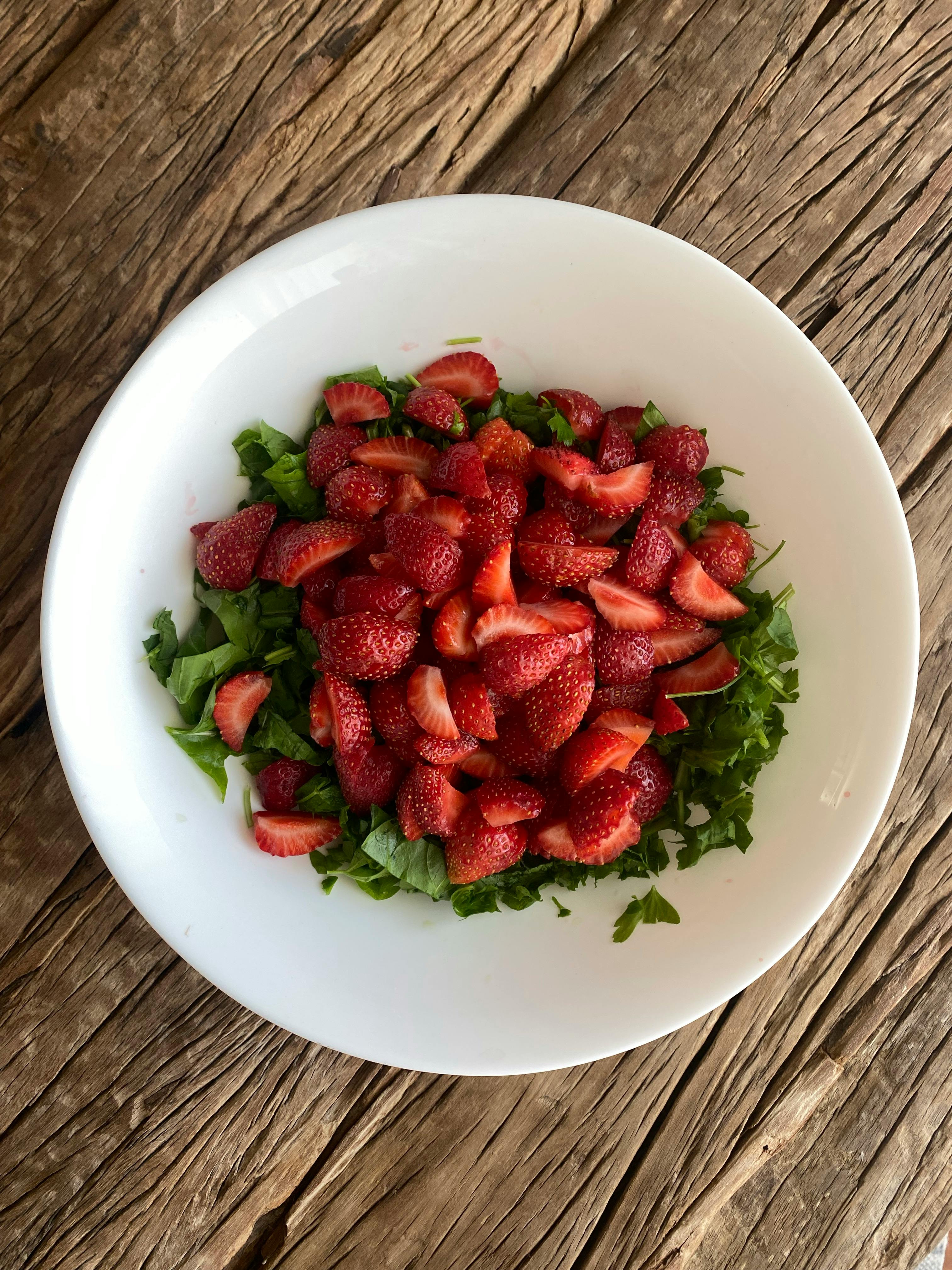 Delicious fresh strawberry salad served in a white bowl on a rustic wooden table.