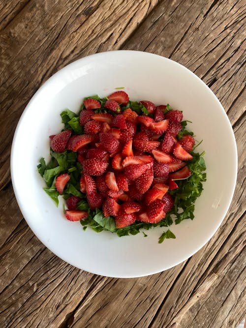 A bowl of strawberries and kale on a wooden table