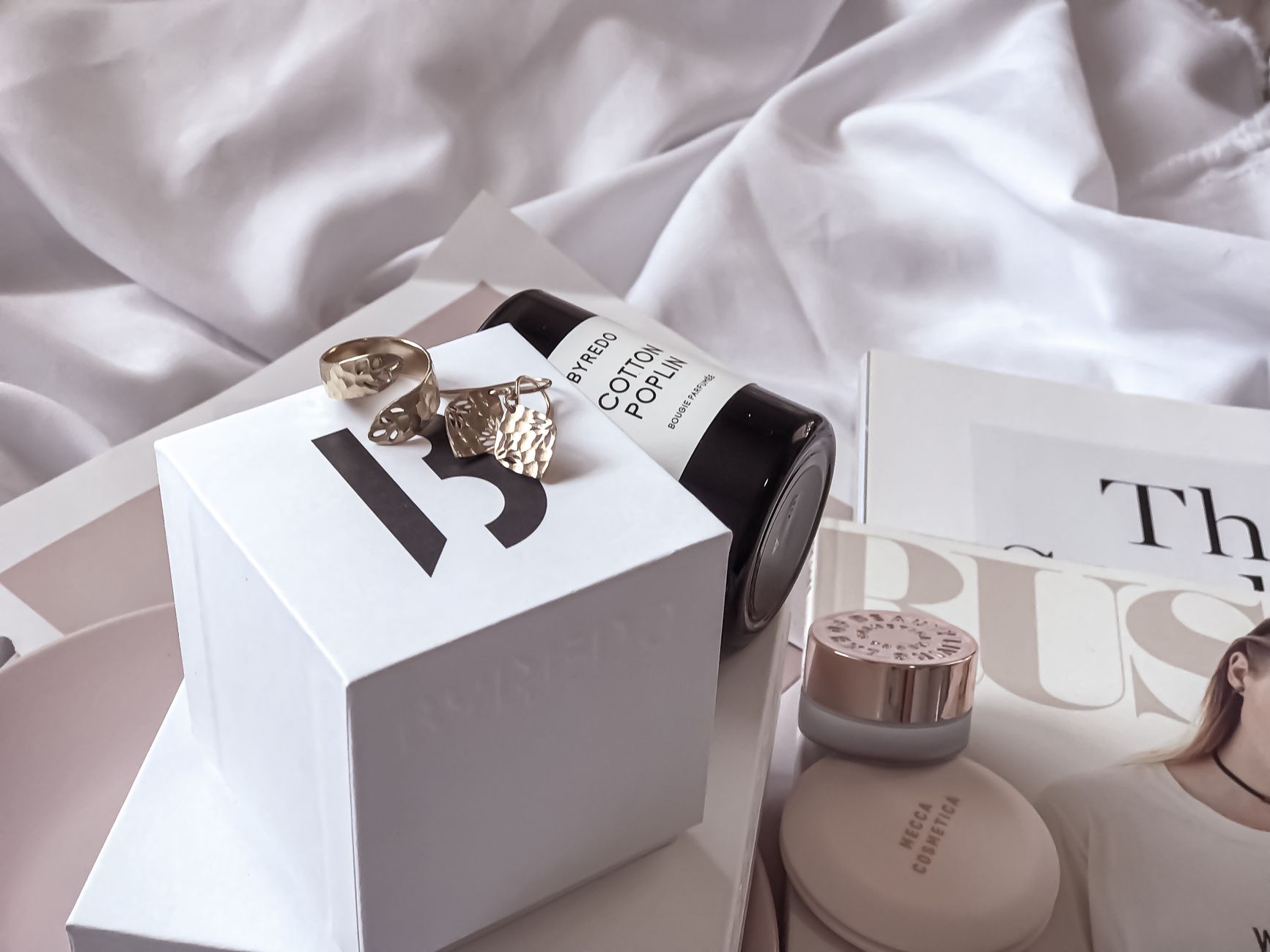Scuffed gold lipstick and jewellery laid across a white sheet, echoing the drawer-dwelling glamour of an old beauty favourite.