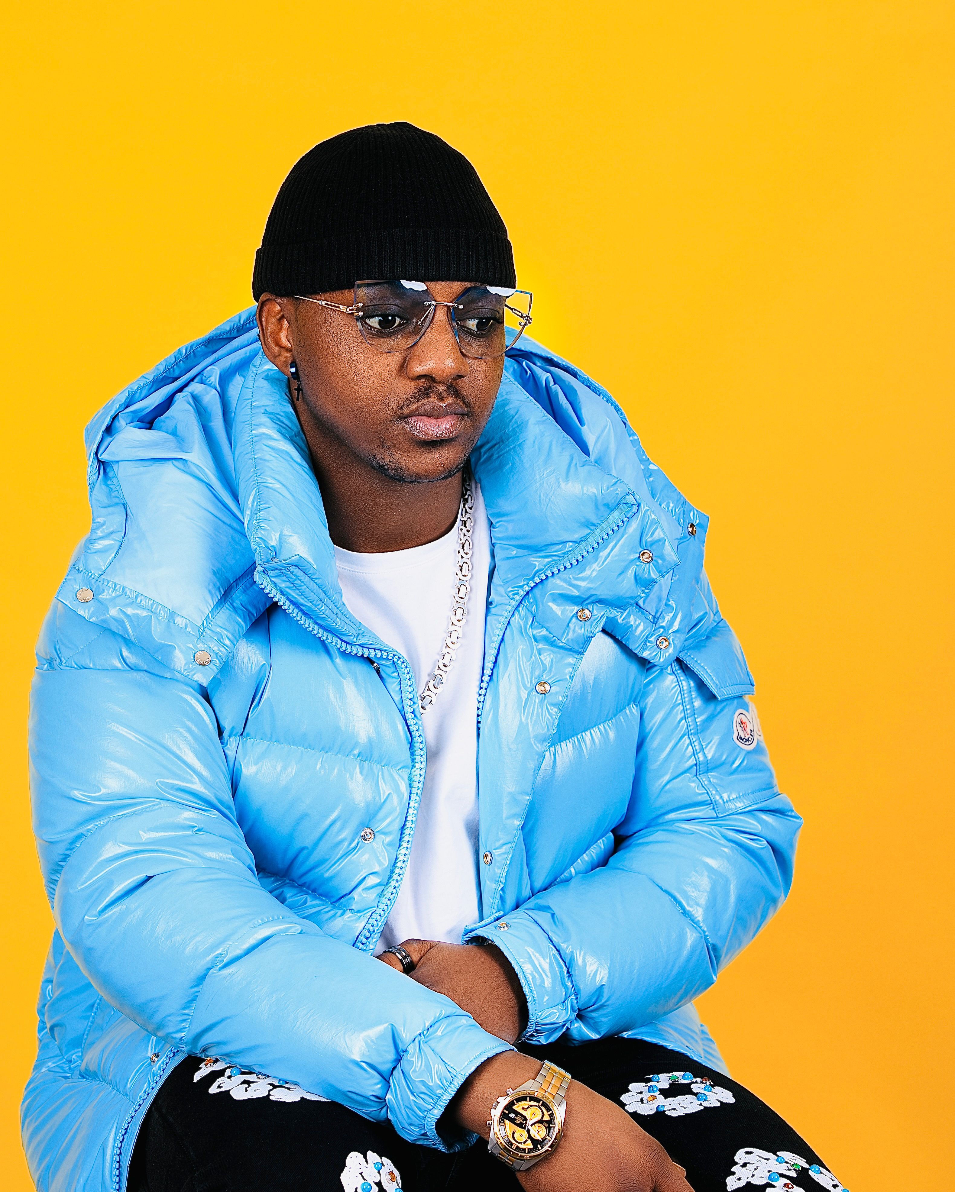 Stylish young man in a blue puffer jacket with a vibrant yellow background.