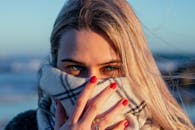 一位有着明亮绿眼和金色头发的女子，戴着围巾，身处户外